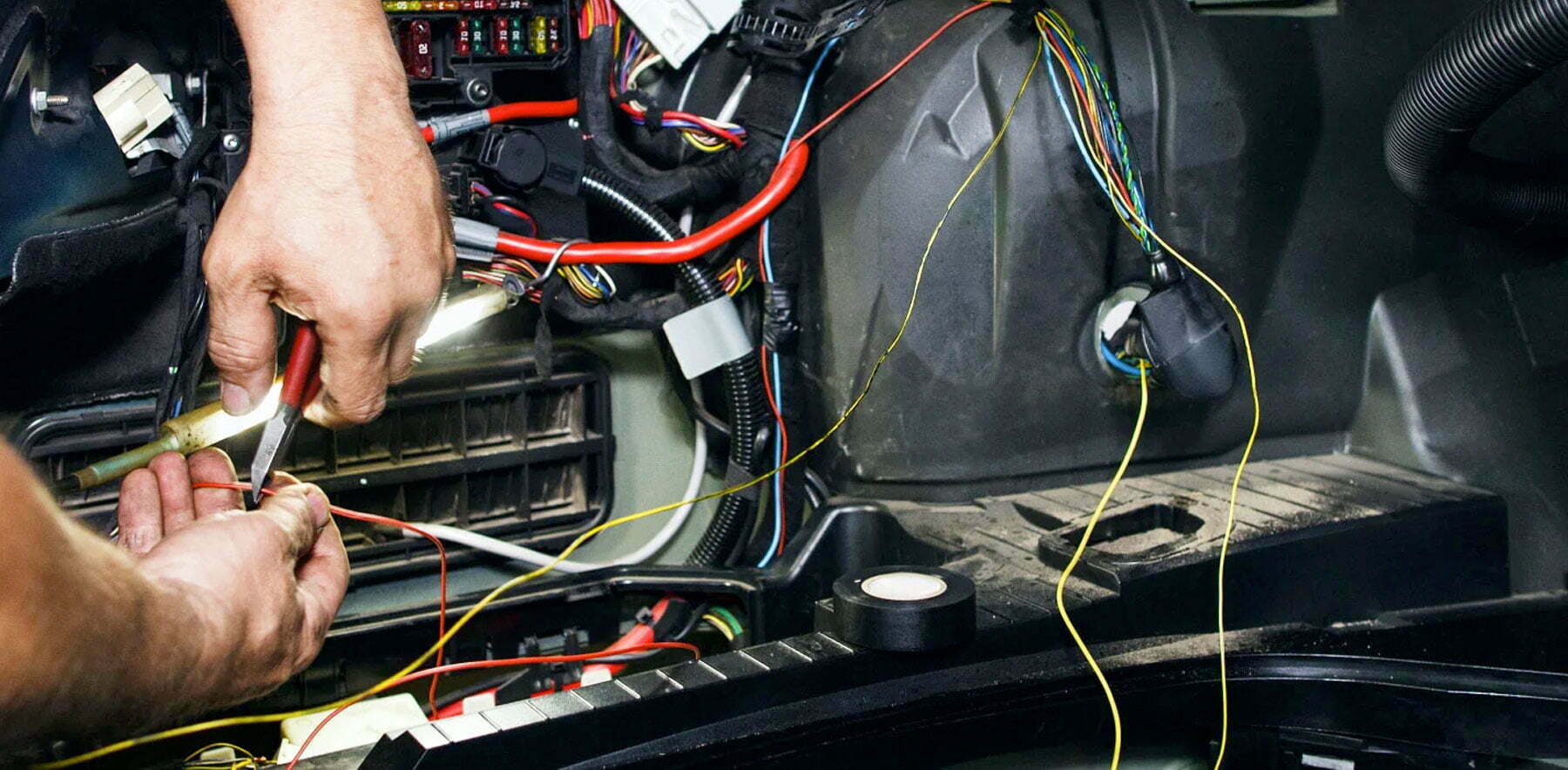 hands repairing a car harness by cutting a wire with plyers