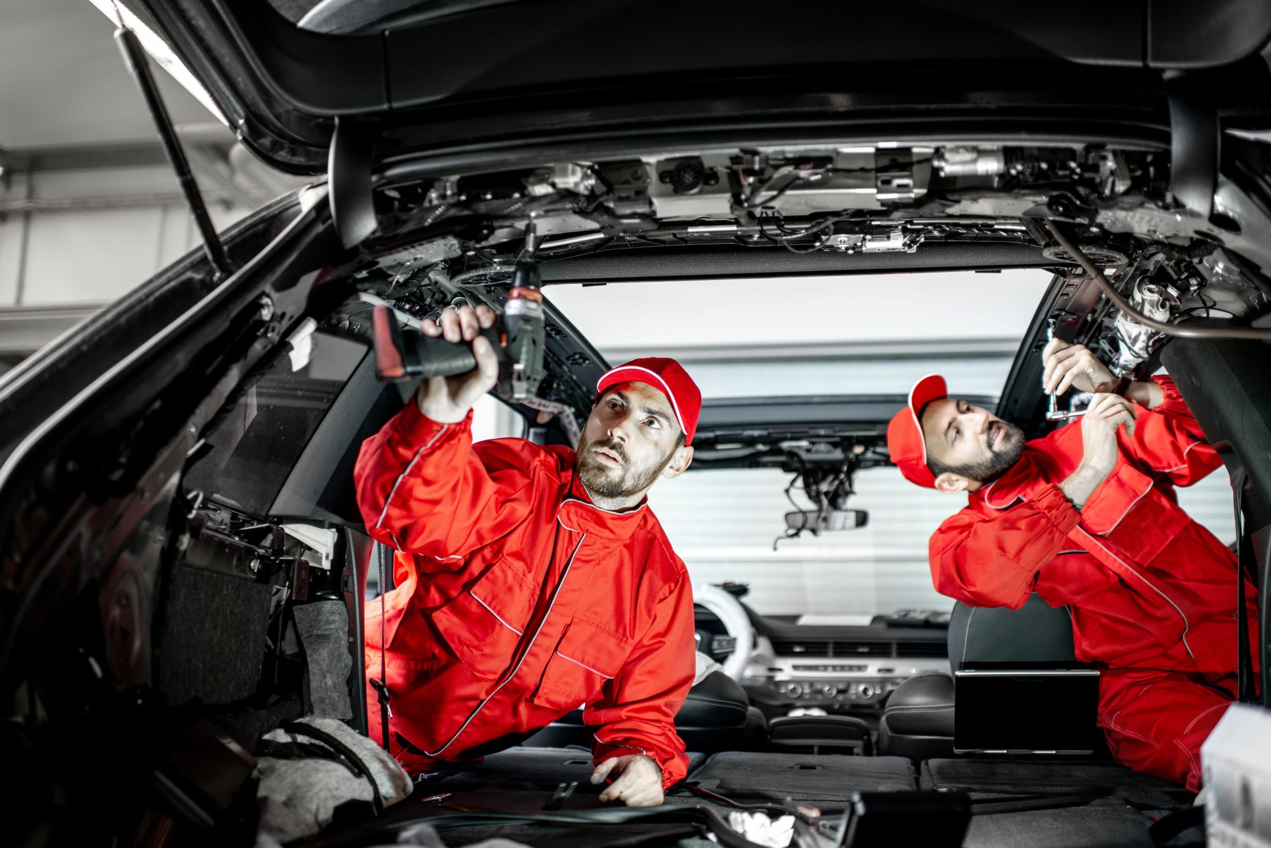 Car service workers disassembling car interior Two auto service workers in red uniform disassembling new car interior making some improvements indoors